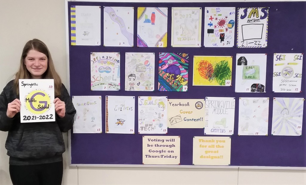 A student holds her winning design with other yearbook cover designs.